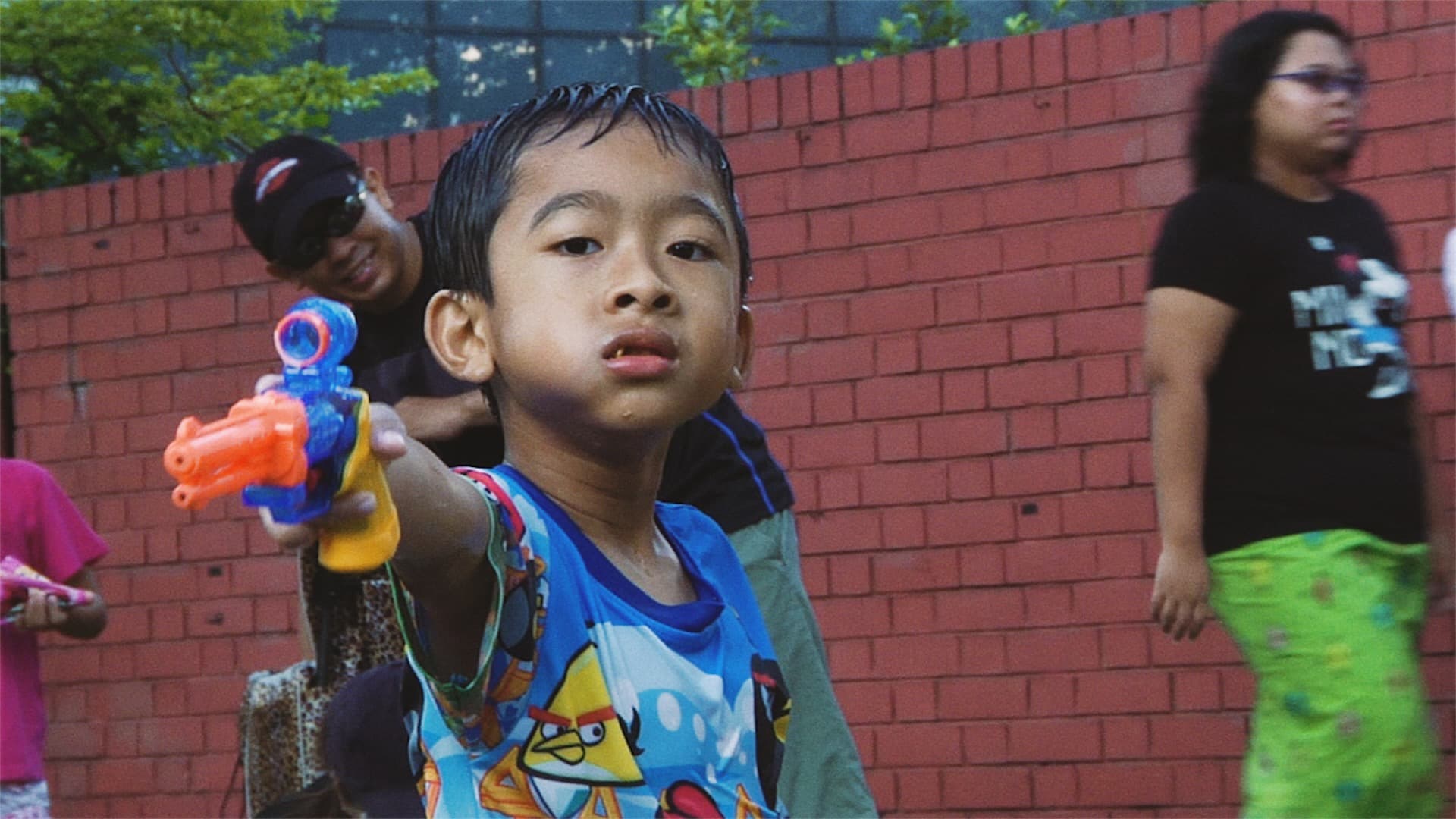 A child points a toy water gun in front of a red wall in SEMENTARA.
